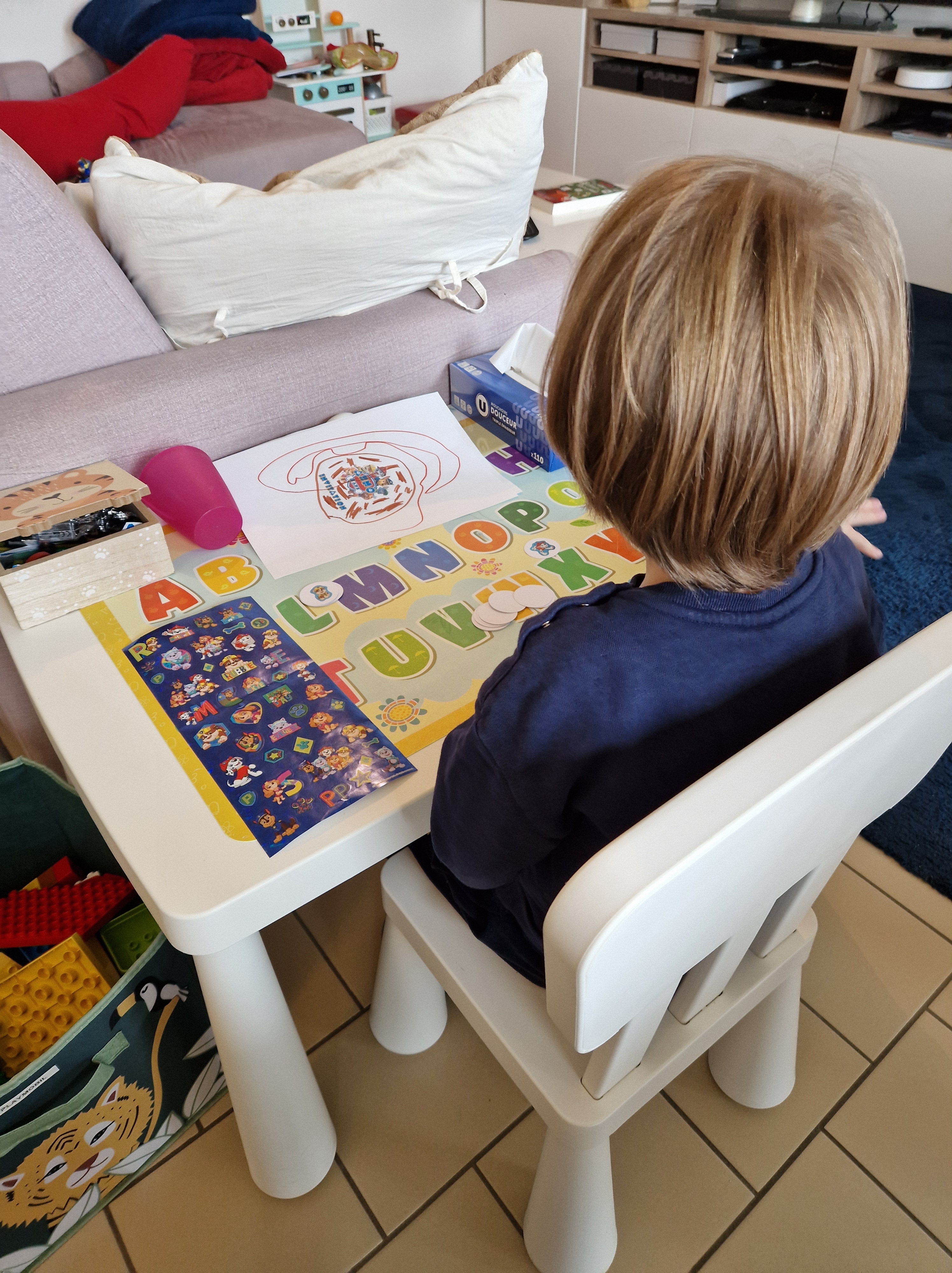 Enfant qui colle les gommettes Pat'Patrouille sur les ronds de papier, vu de dos